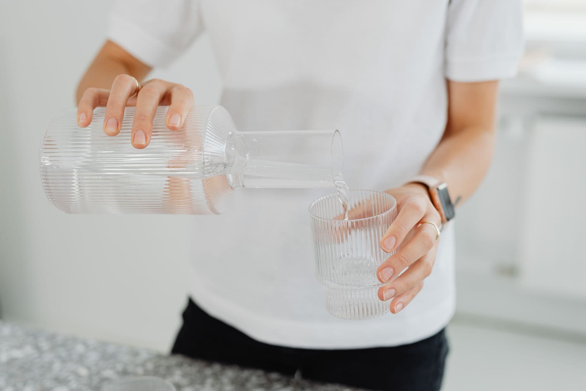 Pouring filtered drinking water from a carafe into a glass on a kitchen counter